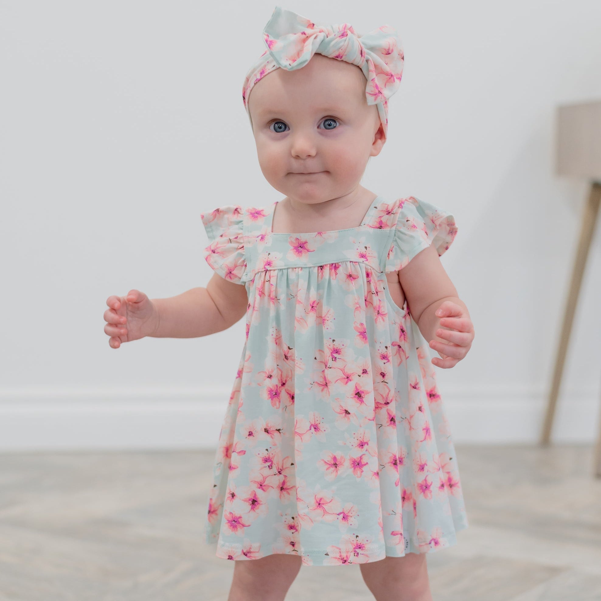 Baby wearing a floral dress and headband on a plain background