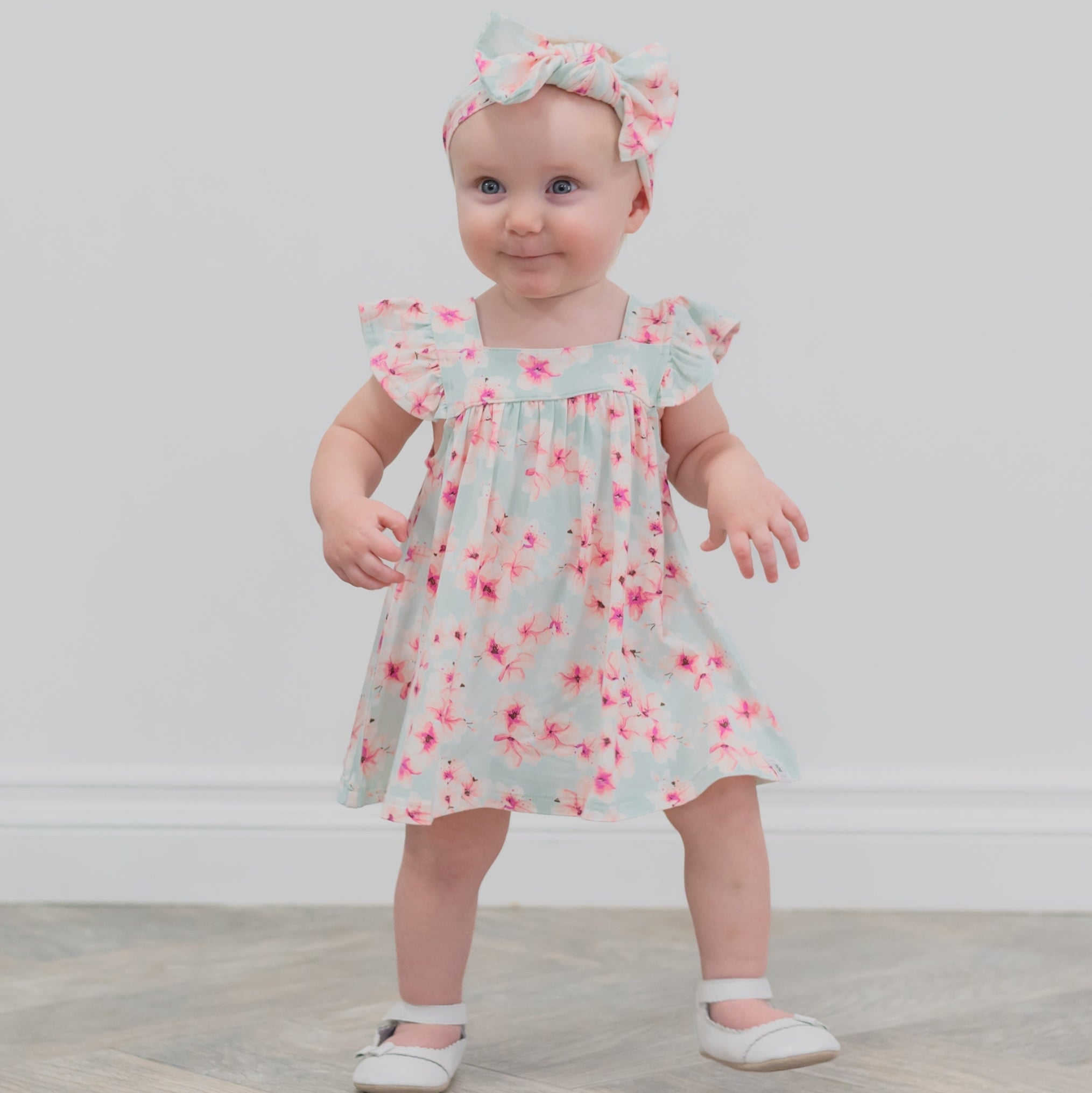 Baby wearing a floral dress and headband on a plain background