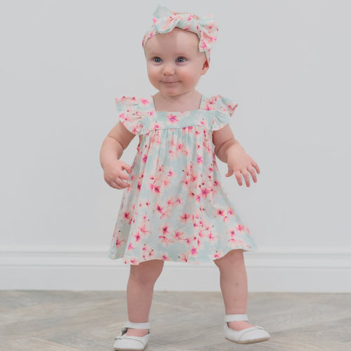 Baby wearing a floral dress and headband on a plain background