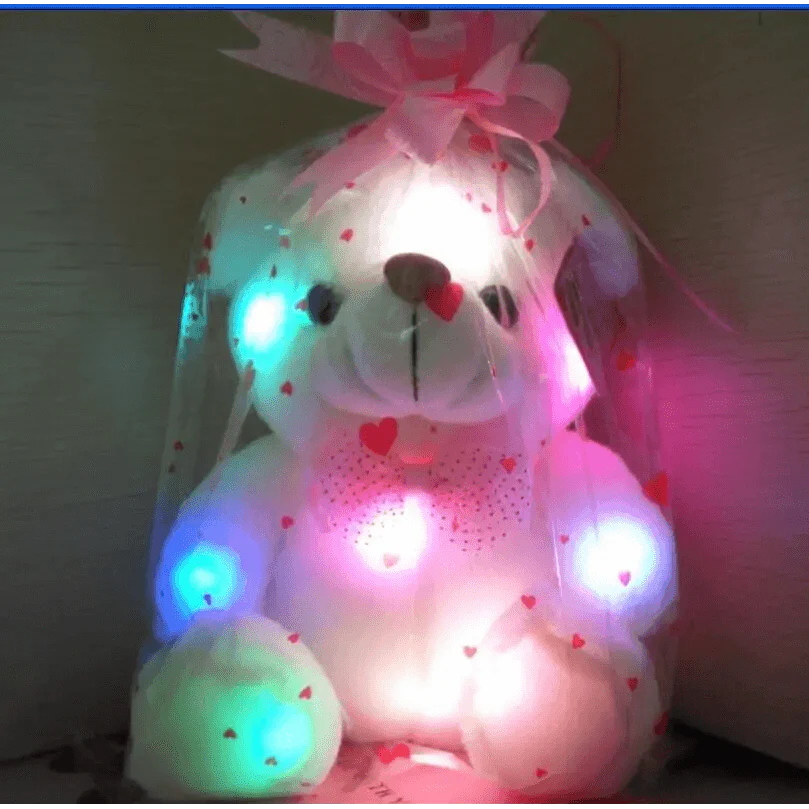 Light-up teddy bear with colorful LEDs inside a sheer white bag on a wooden surface.