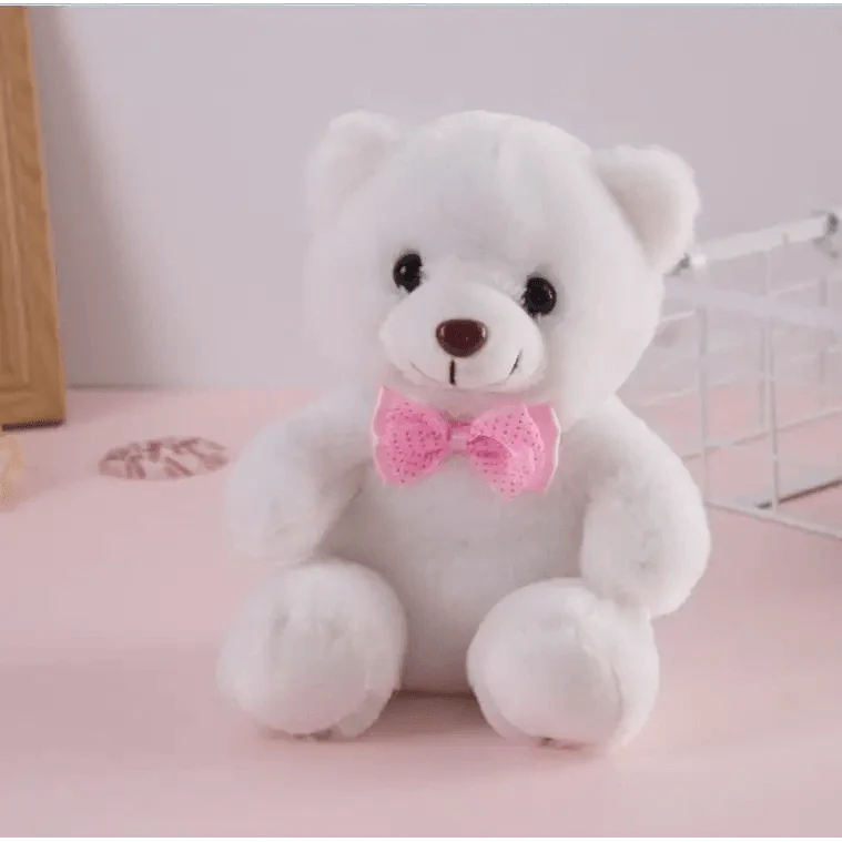 White teddy bear with a pink bow tie on a pink surface