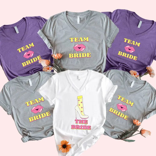 Collection of 'Team Bride' shirts in various colors on a pink background with flowers.
