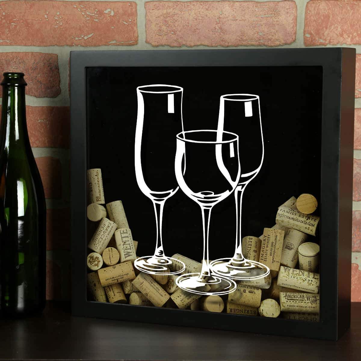 Decorative shadow box with wine glasses and corks against a brick wall.