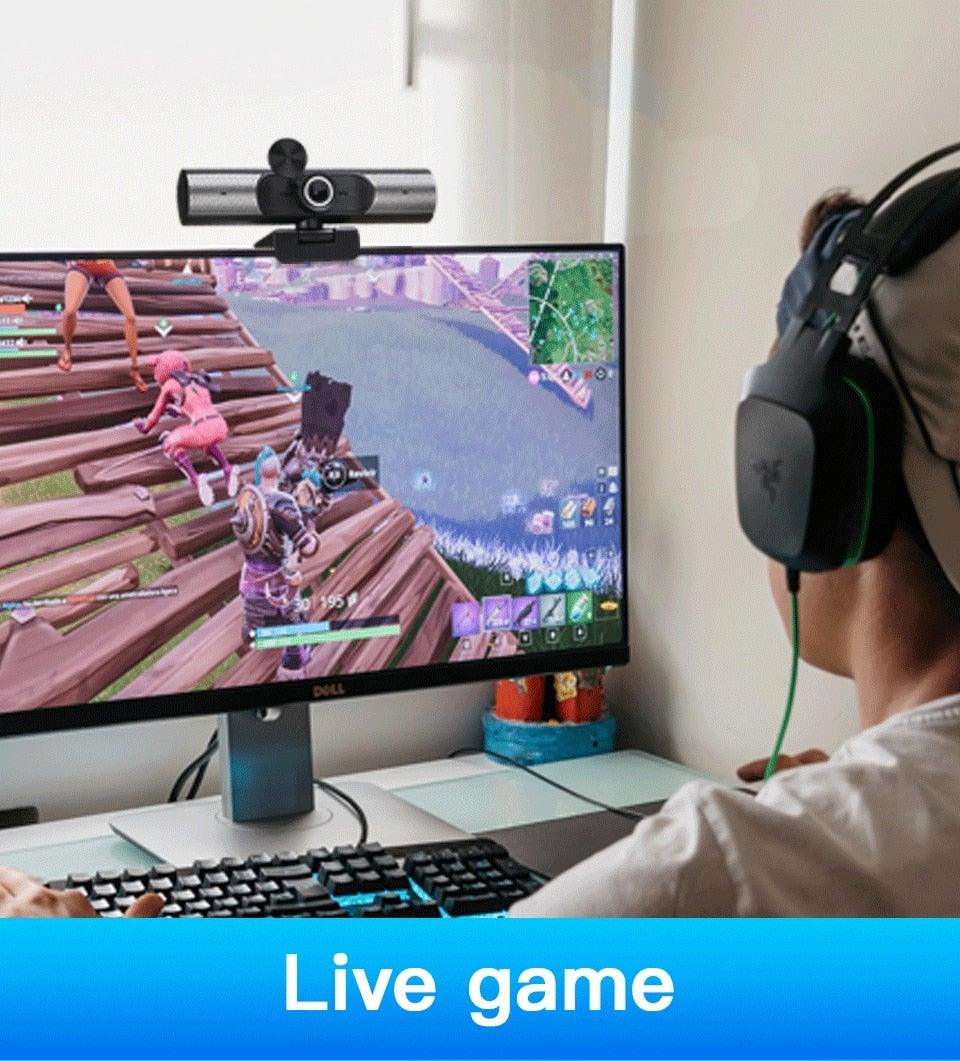 Person playing a game on a computer with a webcam and headphones, sitting at a desk.
