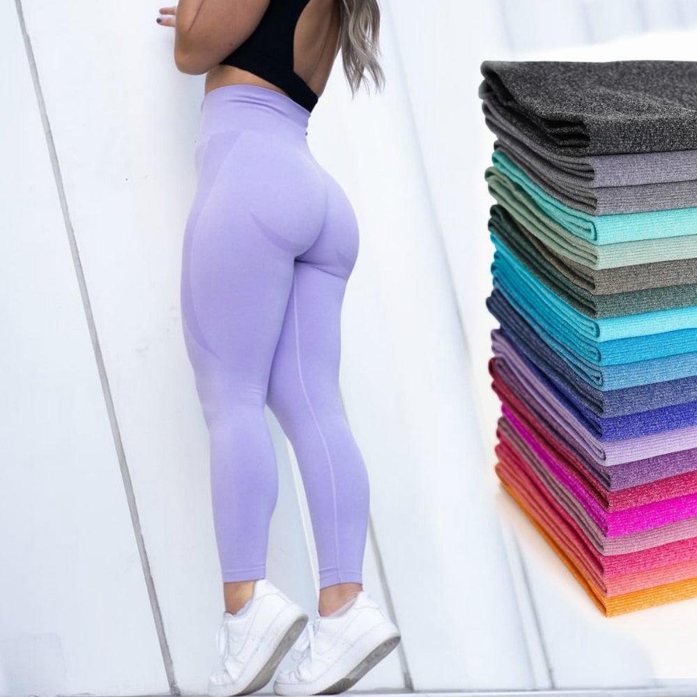 Purple leggings worn by a person with a stack of colorful leggings on a white background
